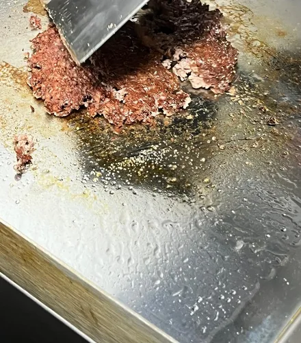 Ein Smash-Patty wird mit dem Spatel auf die heiße Platte gedrückt